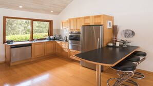 A modern kitchen with wooden cabinets, stainless steel appliances, a black countertop, and a view of greenery outside. - Yallingup Retreat - *Romantic, overlooking a lake, secluded* (YALLINGUP)