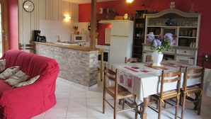 Un salon confortable avec un canapé rouge, une table à manger avec des chaises, un coin cuisine équipé d’une cuisinière et d’un réfrigérateur.
