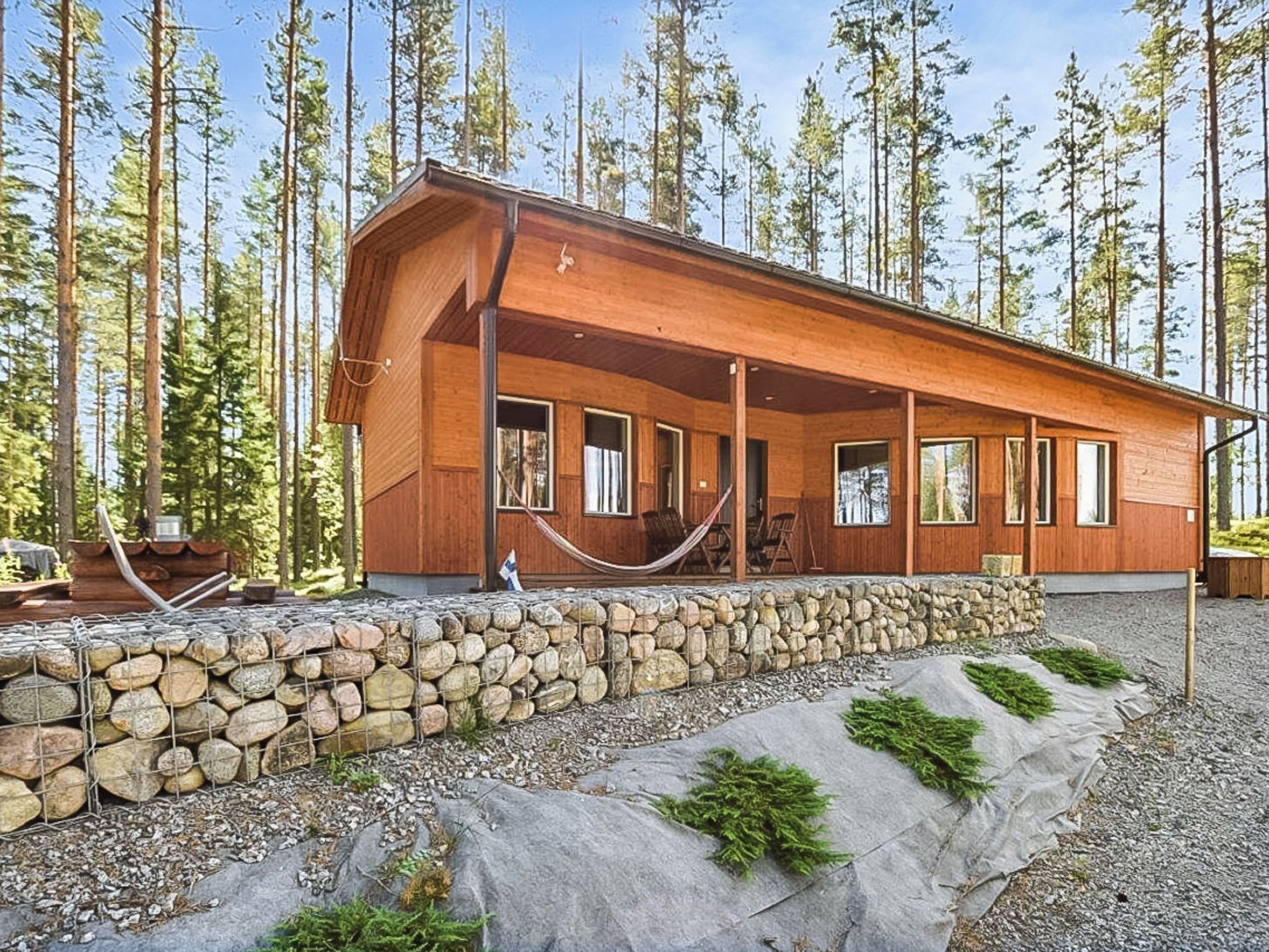 Una cabaña de madera con base de piedra, ventanas amplias y un porche con sillas.
