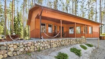 Una cabaña de madera con base de piedra, ventanas amplias y un porche con sillas.