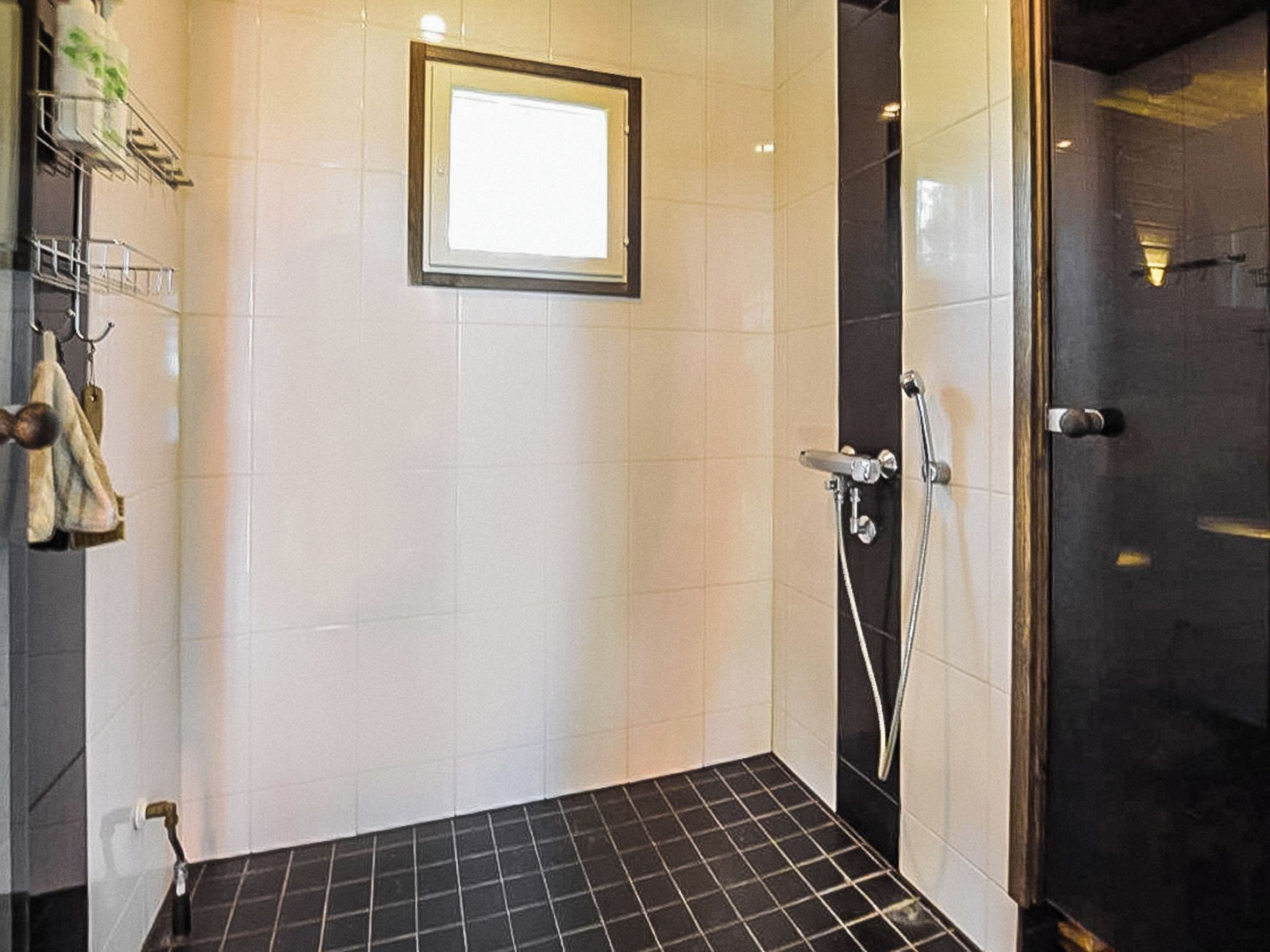 Ein kleines Duschbad mit gefliesten Wänden, einer Glasduschkabine, einem Handtuchhalter mit Handtüchern und einem kleinen Fenster.