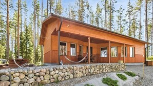 Eine Holzhütte mit Steinfundament, großen Fenstern und einer Veranda mit Stühlen.