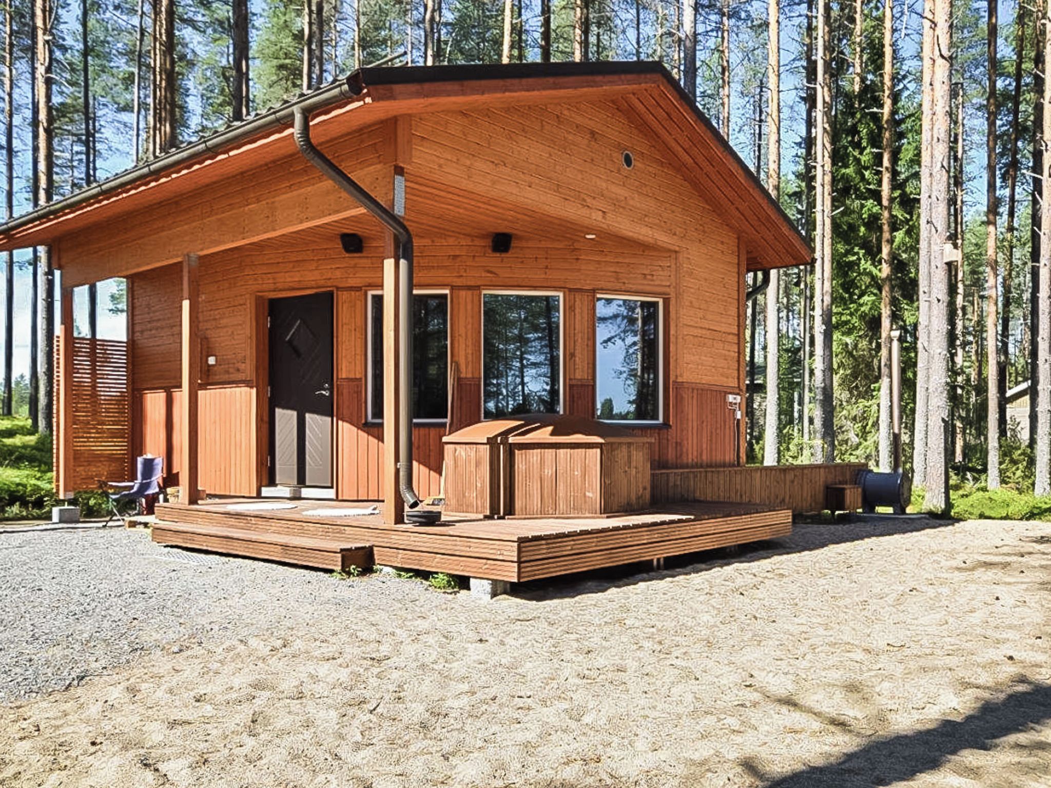 Puinen mökki, jossa on katettu kuisti, suuret ikkunat ja terassi.