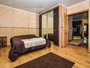 Een slaapkamer met een groot bed, een houten vloer, een schuifdeur naar een badkamer en een klein nachtkastje.