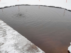 Een groot, rond, donker waterlichaam met een bevroren rand, omgeven door sneeuw.
