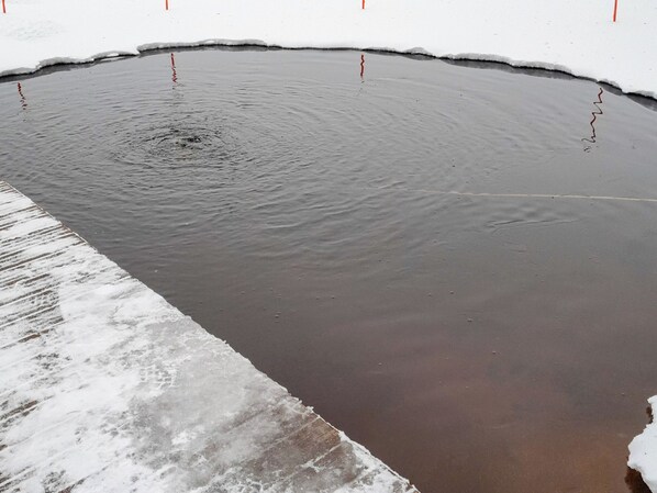 A large, circular, dark-colored water body with a frozen edge, surrounded by snow.