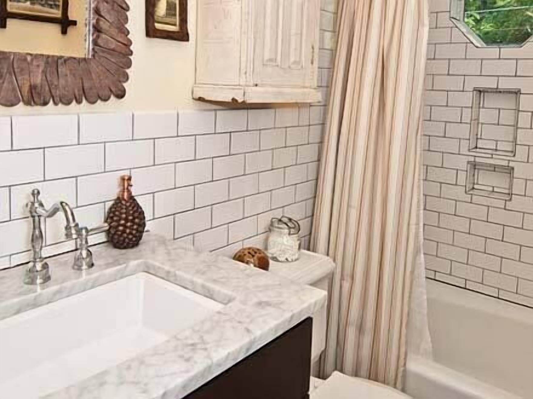 A bathroom with a white tiled wall, a sink with a marble countertop, a shower with a glass door, and a towel rack.