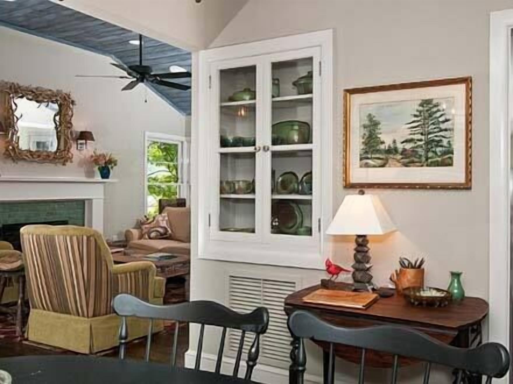 Un salon chaleureux avec une cheminée, une table à manger avec des chaises, un ventilateur de plafond et un meuble avec des portes en verre.