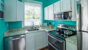 Una cocina moderna con armarios blancos, electrodomésticos de acero inoxidable y una ventana con persianas.