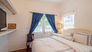 Un dormitorio con cama, una silla, televisor, lámpara y ventana con cortinas.