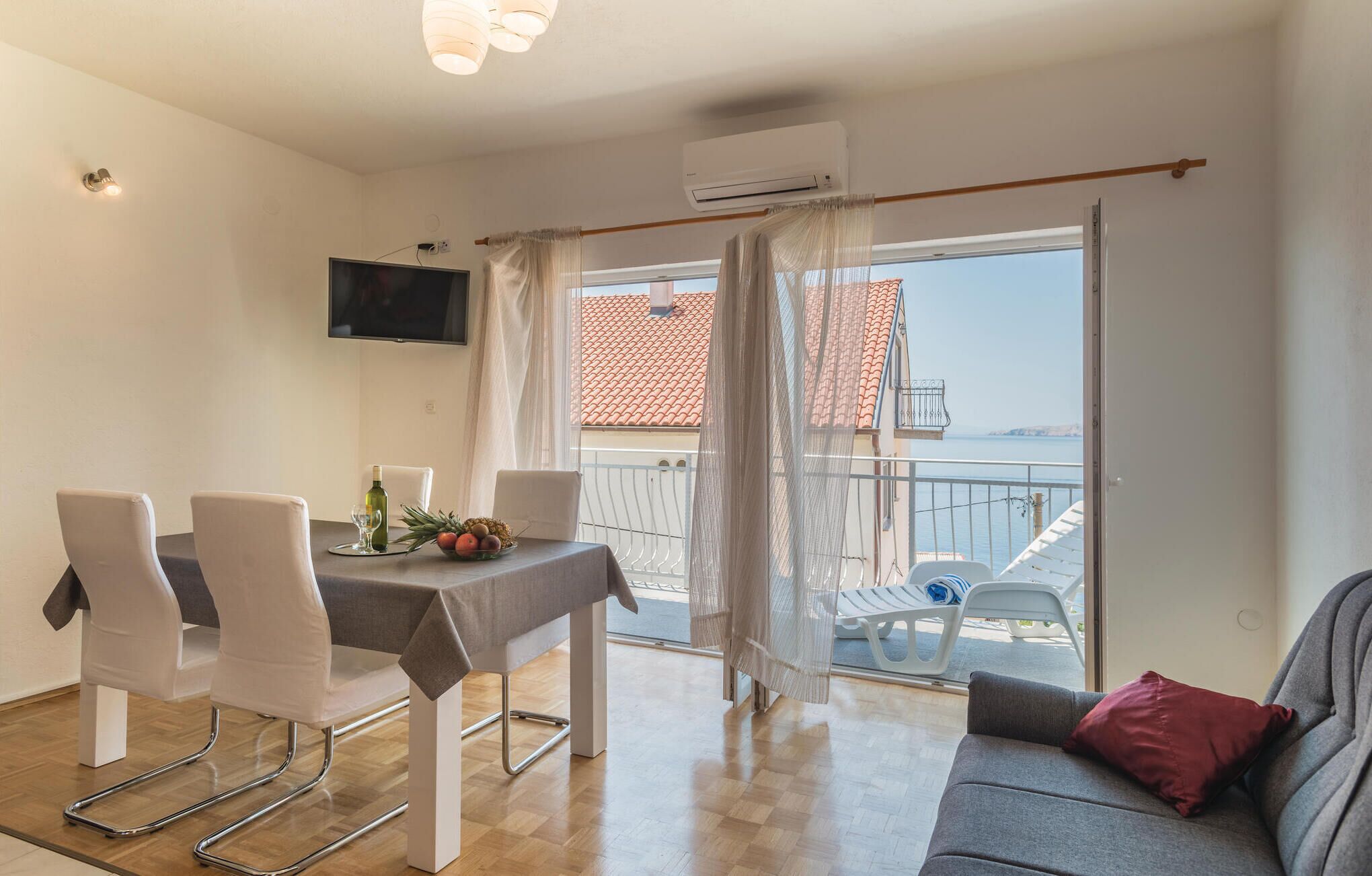 Ein Essbereich mit Tisch und Stühlen, einem an der Wand montierten Fernseher und einem Balkon mit Meerblick.