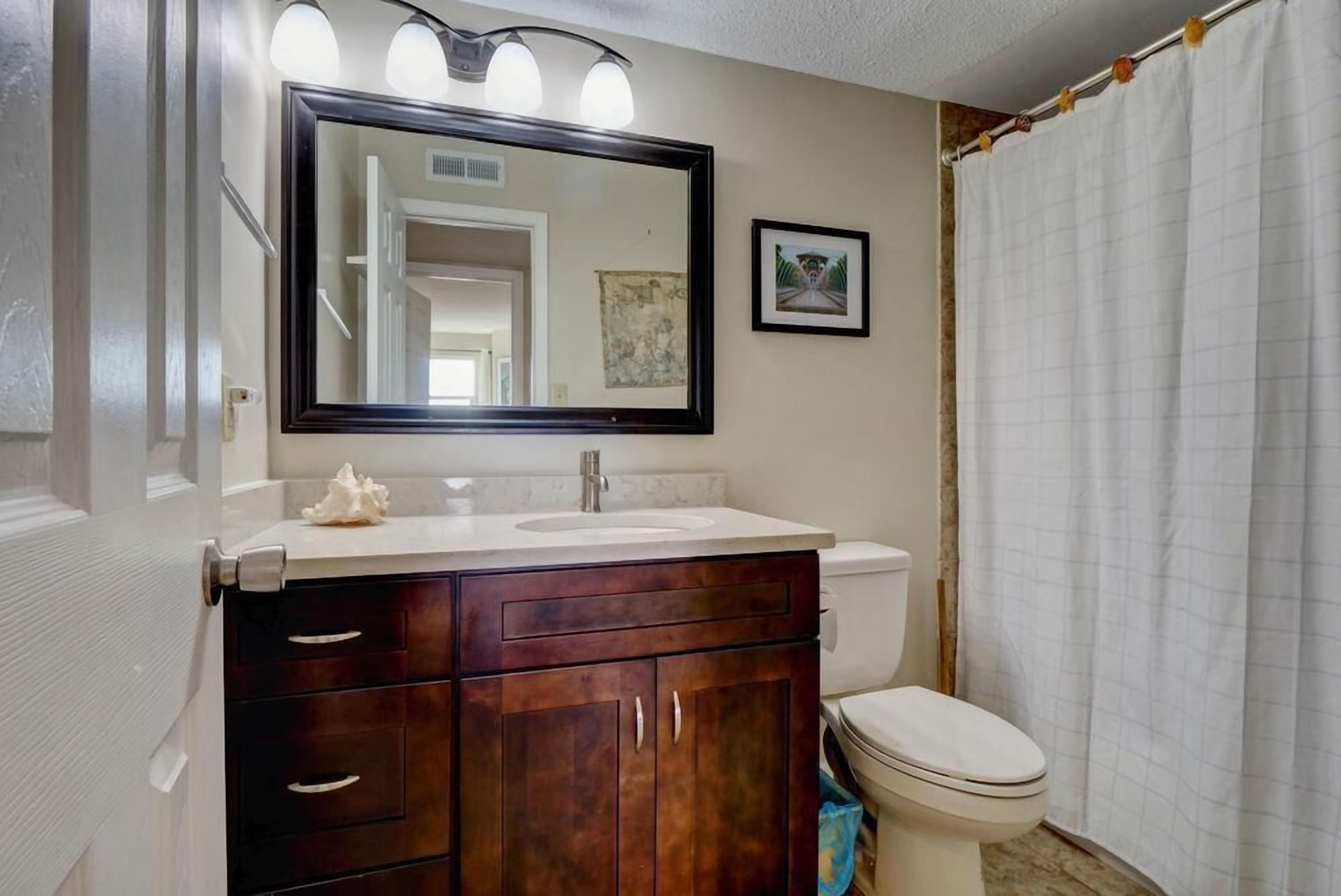 A bathroom with a dark wooden vanity, a white sink, a large mirror, and a white toilet.