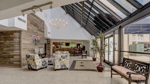 Eine geräumige Lobby mit hoher Decke, einem Kronleuchter, einer Sitzecke mit Sofas und einer Bank sowie einem großen Fenster mit Außenblick.