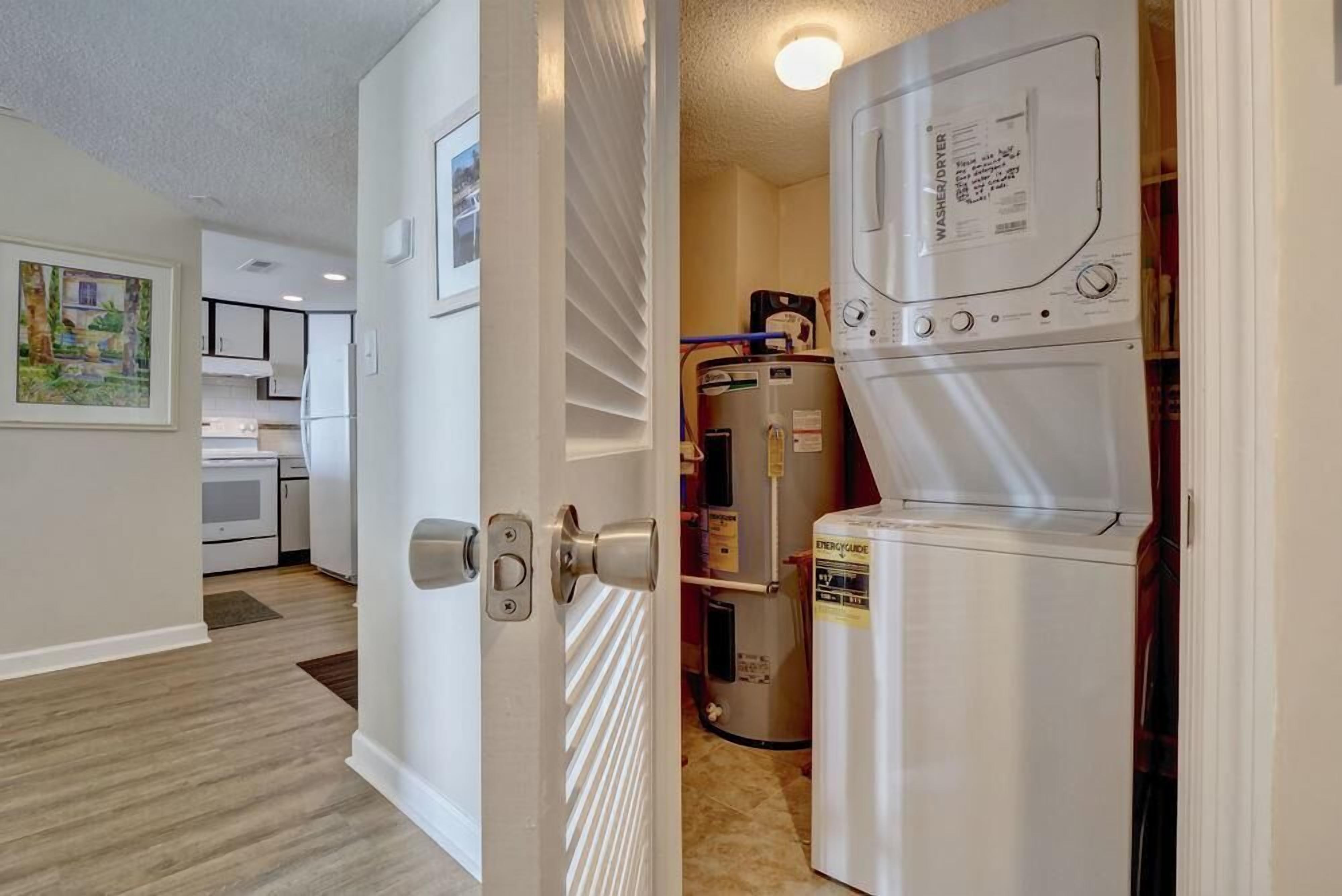 A laundry room with a washer and dryer, a water heater, and a kitchen area visible through an open door.