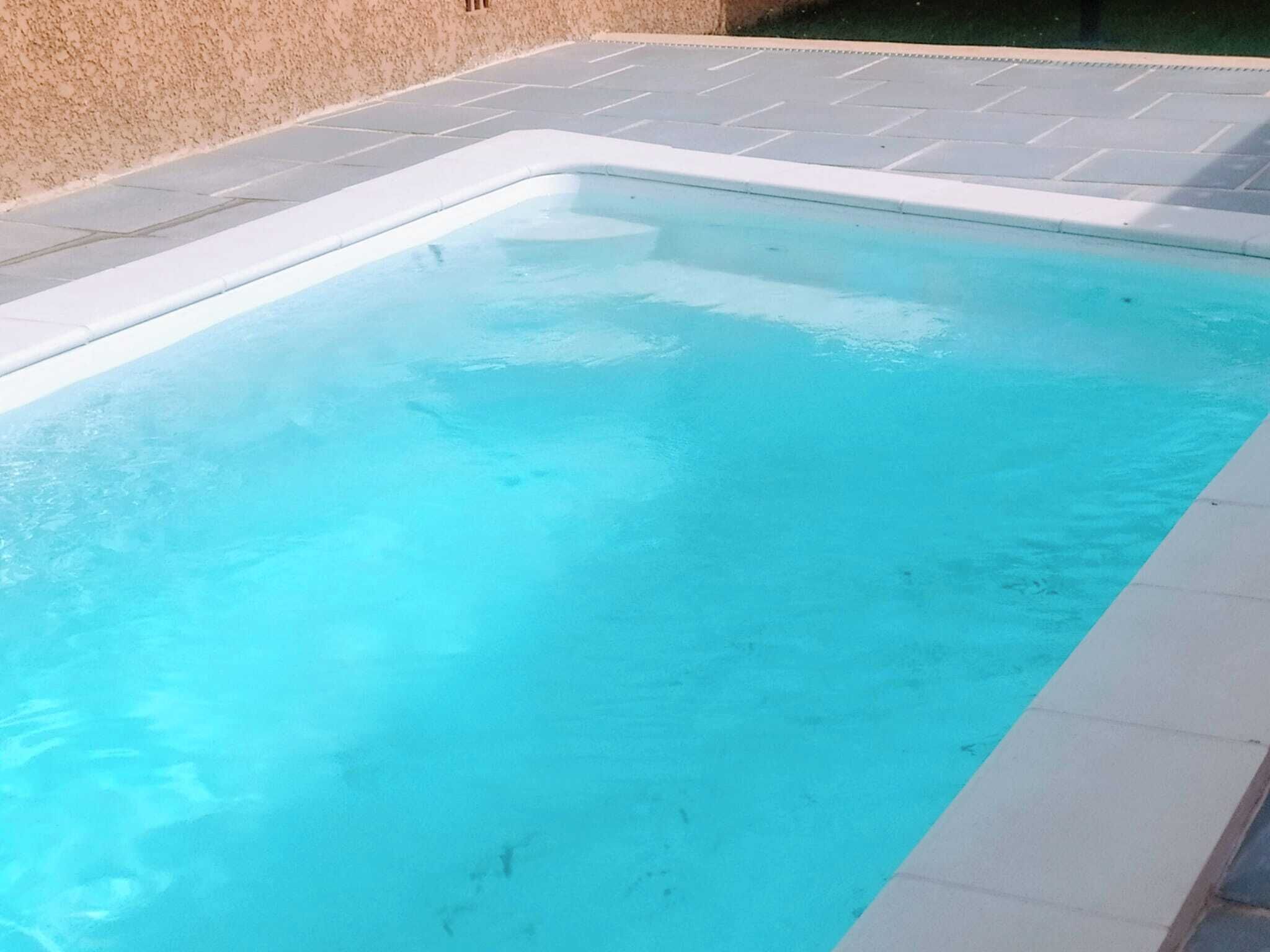 Une piscine rectangulaire dont le bord est revêtu de carreaux, entourée d’une terrasse en béton.