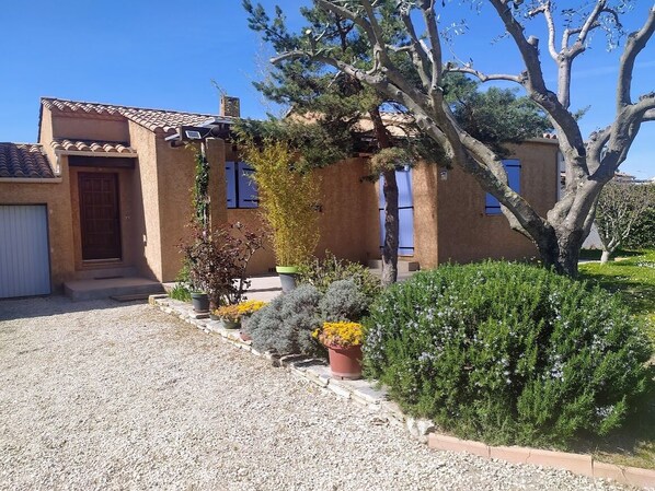 A house with a gravel driveway, a wooden door, and a window with a white curtain.
