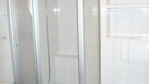Moderni kylpyhuone, jossa on lasiseinällä erotettu suihku, valkoiset laatat ja näkyvissä oleva wc-istuin.
