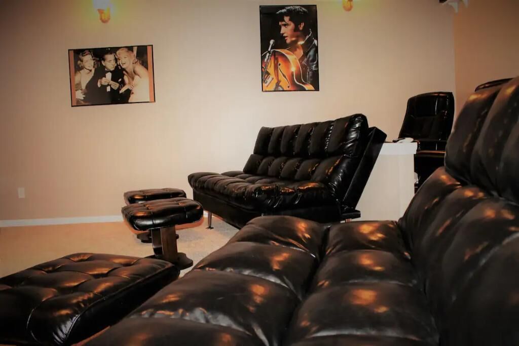 A room with a black leather sofa, a black leather ottoman, and a massage chair. There are two framed pictures on the wall.