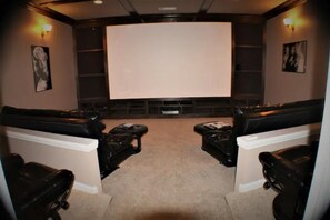 Una sala de cine en casa con una pantalla grande, asientos de cuero negro y piso alfombrado.