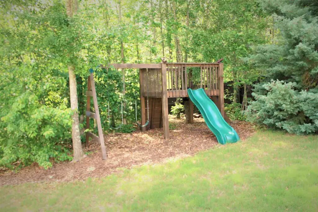 A wooden play structure with a slide in a wooded area.