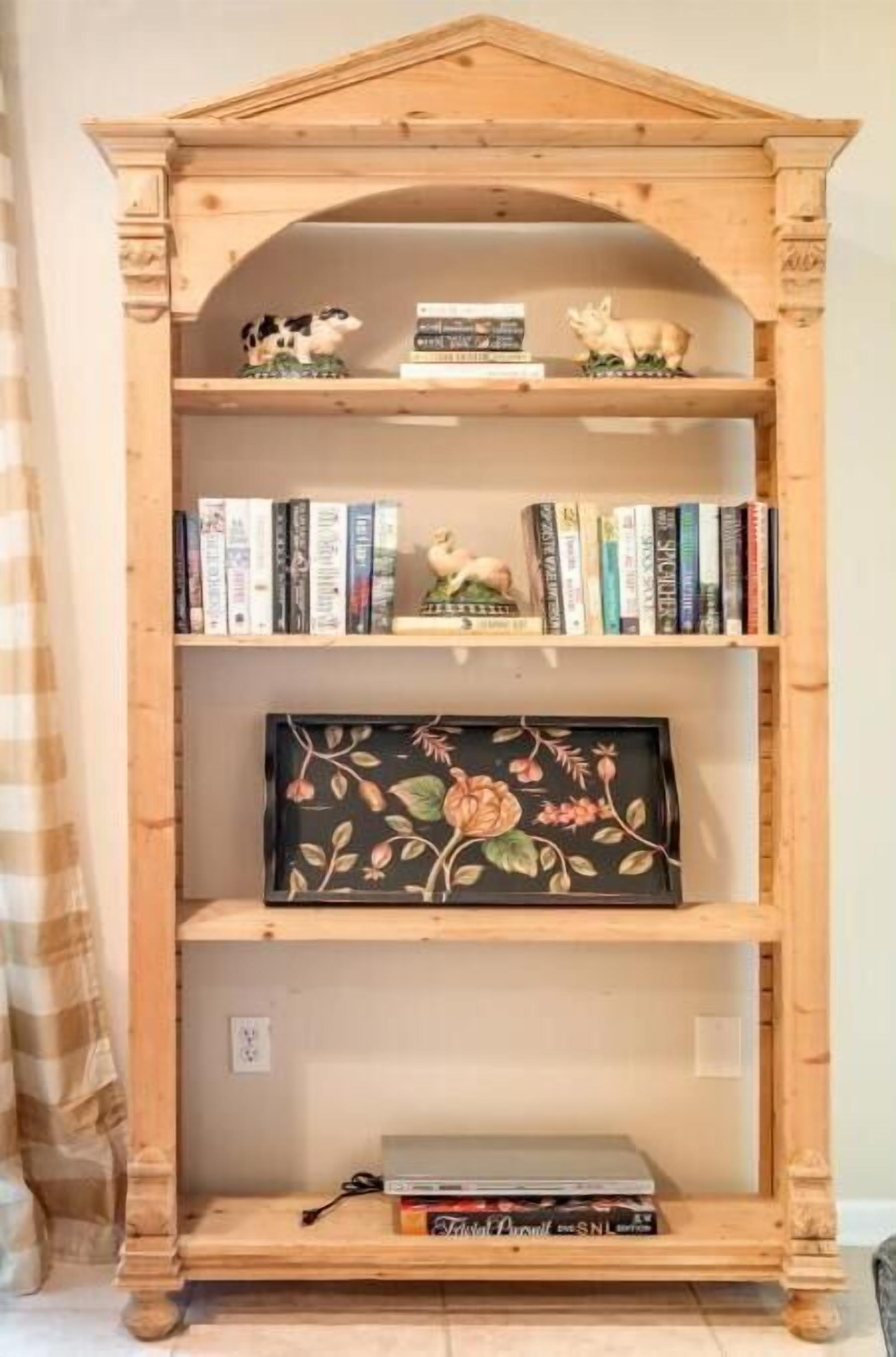 Uma estante de madeira com três prateleiras, cada uma contendo livros e objetos decorativos.