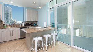 A modern kitchen with granite countertops, a coffee maker, and a view of a cityscape through large windows. - Lovely 4th Floor Condo at the Sapphire! Resort Pool, Hot Tub, Spa, Movie Theater & More! (South Padre Island)