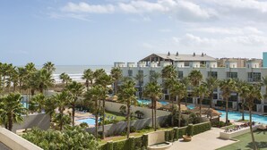 A resort with a pool area, palm trees, and a view of the ocean. - Lovely 4th Floor Condo at the Sapphire! Resort Pool, Hot Tub, Spa, Movie Theater & More! (South Padre Island)