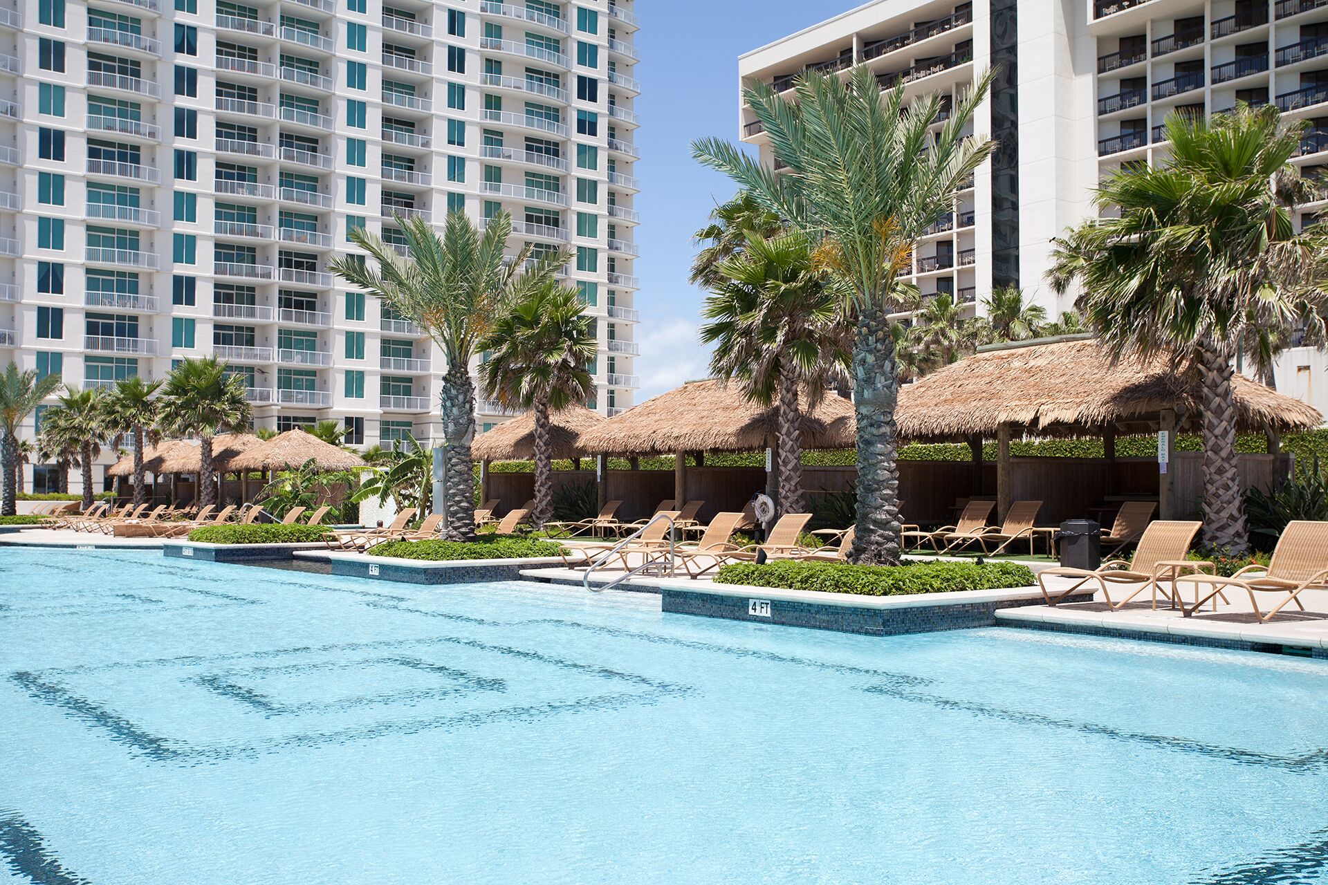 A hotel pool area with lounge chairs and palm trees, surrounded by high-rise buildings.