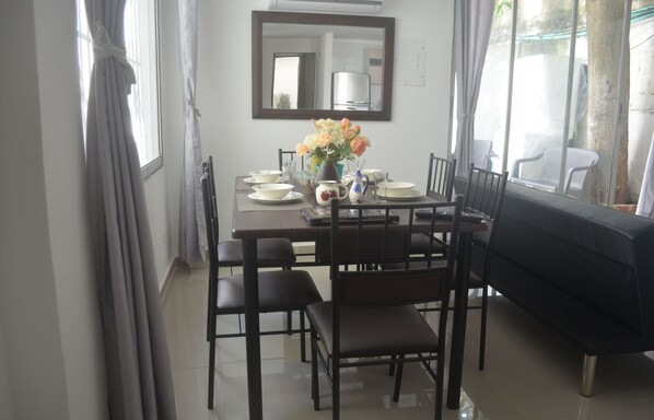 A dining area with a table set for four, chairs, a vase with flowers, and a sofa. - Casitas Cartagena by Castillo Grande Beach (Cartagena)