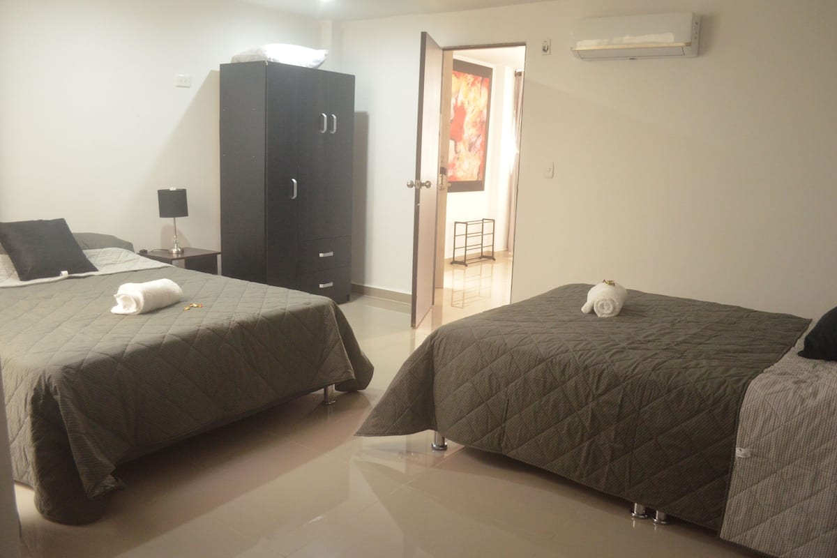 A hotel room with two beds, a wardrobe, a nightstand, and a door leading to a hallway.