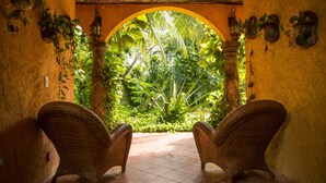 A room with two wicker chairs facing a large arched window overlooking a lush garden.