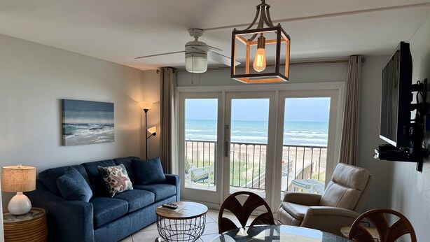 A living room with a sofa, a glass-top dining table, and chairs, a ceiling fan, and a view of the ocean through large windows. - Private 2nd floor balcony facing the Gulf, sleeps 6. Pool & hot tub (South Padre Island)