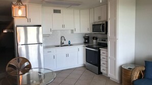 A modern kitchen with white cabinets, stainless steel appliances, a glass dining table, and a wicker chair. - Private 2nd floor balcony facing the Gulf, sleeps 6. Pool & hot tub (South Padre Island)