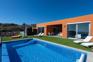 A modern house with a swimming pool, outdoor seating, and a view of the hills.