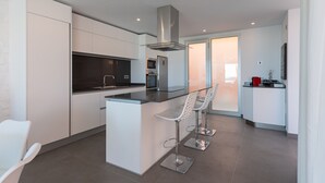 A modern kitchen with white cabinetry, a central island with bar stools, and a stainless steel range hood.