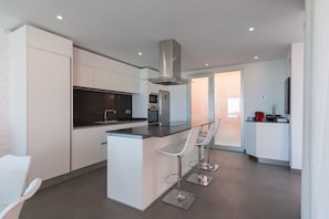 Una cocina moderna con armarios blancos, una isla central con taburetes de bar y una campana extractora de acero inoxidable.