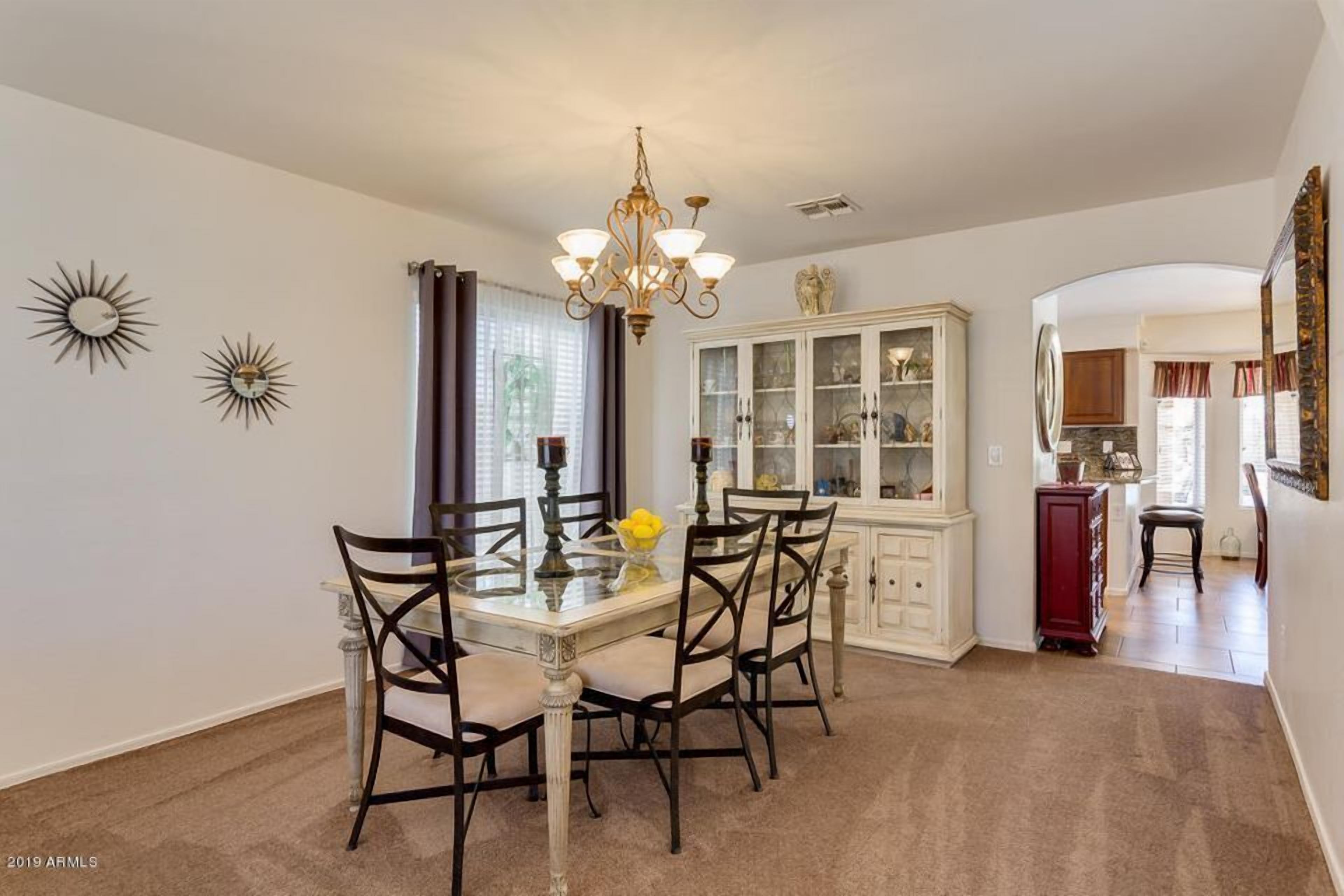 A dining area with a glass table, four chairs, a chandelier, and a cabinet with glass doors.