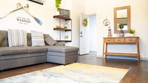 Una sala de estar con un sofá modular, una consola, una estantería montada en la pared y una puerta que da a otra habitación.