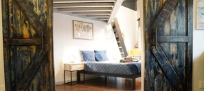 A loft bedroom with a sloped ceiling, a bed with blue bedding, a nightstand, and a ladder leading to an upper level.