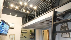 A multi-level interior with exposed ceilings, a staircase, and a television screen. - Rivers Edge Lofts - Unit 4 (Niles)