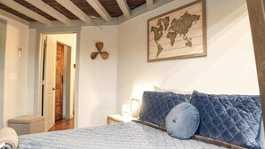 A bedroom with a bed, pillows, a nightstand, a lamp, a wooden ceiling, a door, and a world map on the wall. - Rivers Edge Lofts - Unit 4 (Niles)