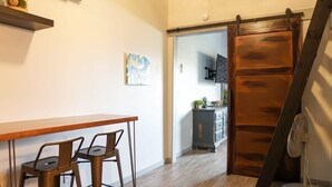 Una habitación con una mesa y sillas de madera, una puerta corredera, un armario pequeño y un ventilador.