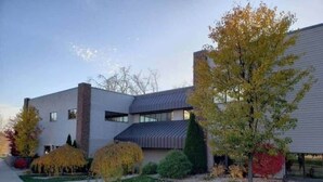 Un edificio moderno con techo plano, chimenea de ladrillo y césped cuidado con árboles de colores otoñales.