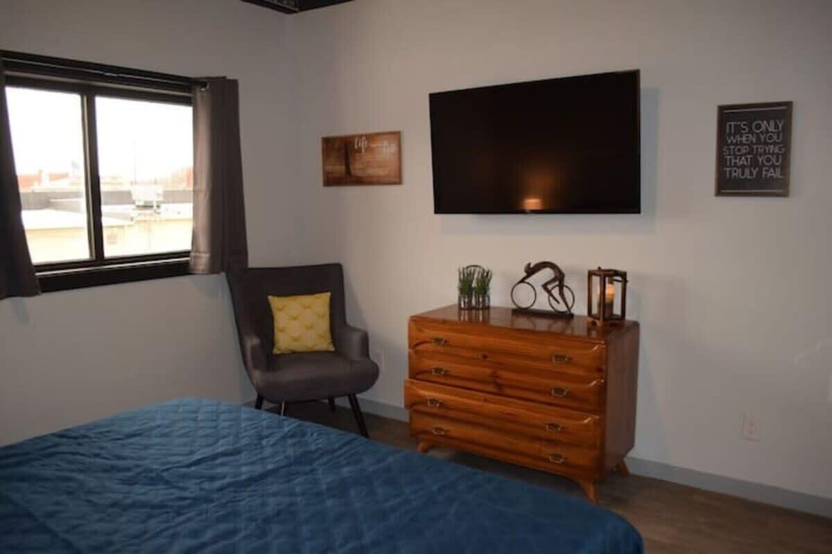 Ein Schlafzimmer mit Bett, Kommode, Stuhl, Fernseher und Fenster.