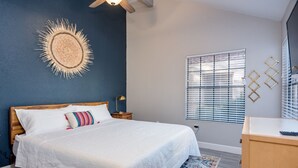 Ein Schlafzimmer mit Bett, Nachttisch, Wanddekoration, Fenster mit Jalousien und Schreibtisch.