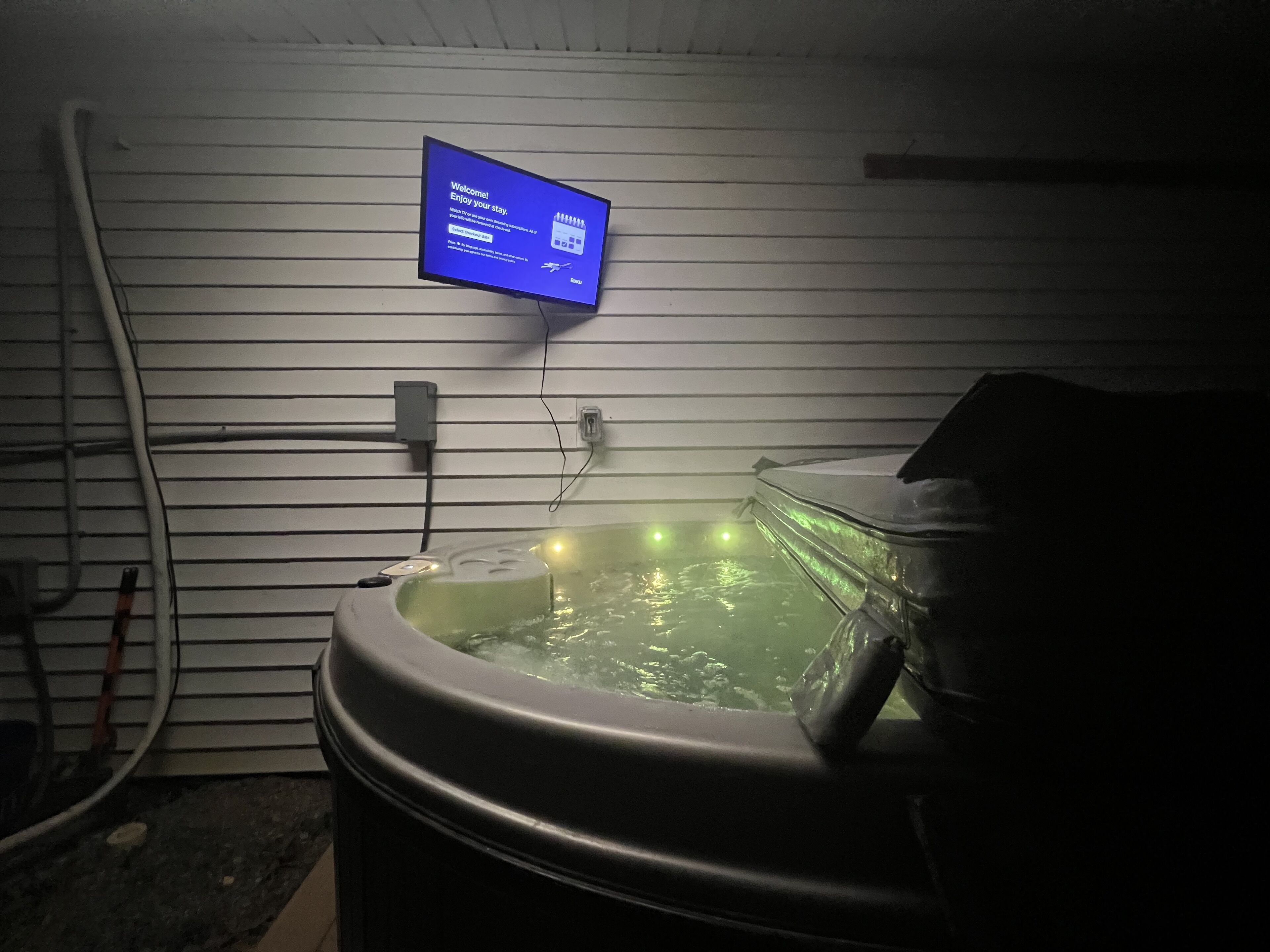 Ein Zimmer mit Whirlpool, einem angebrachten Fernseher, der eine Willkommensnachricht zeigt, und sichtbaren Steckdosen.