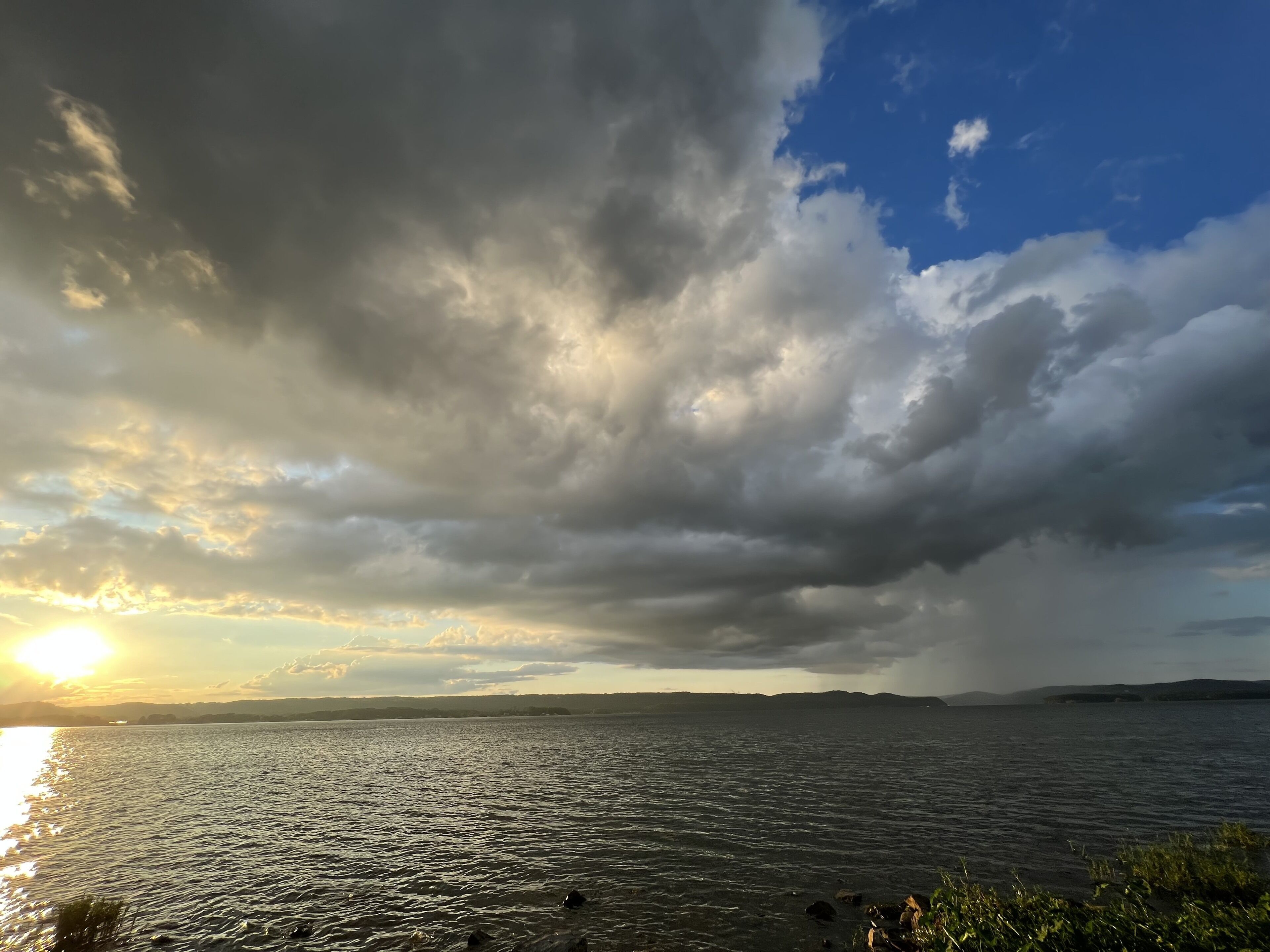 A body of water with a cloudy sky and the sun setting or rising.