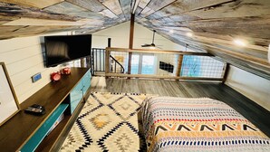 Une chambre de style « loft » avec des poutres apparentes, un téléviseur à écran plat, un tapis à motifs et un lit doté d’une tête de lit colorée.