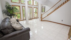 A spacious living area with a leather sofa, large windows, a staircase, and a potted plant. - Oceanside, Pool, Hot Tub, Close to Beach, OH1, Silver Sandcastle (Corolla)