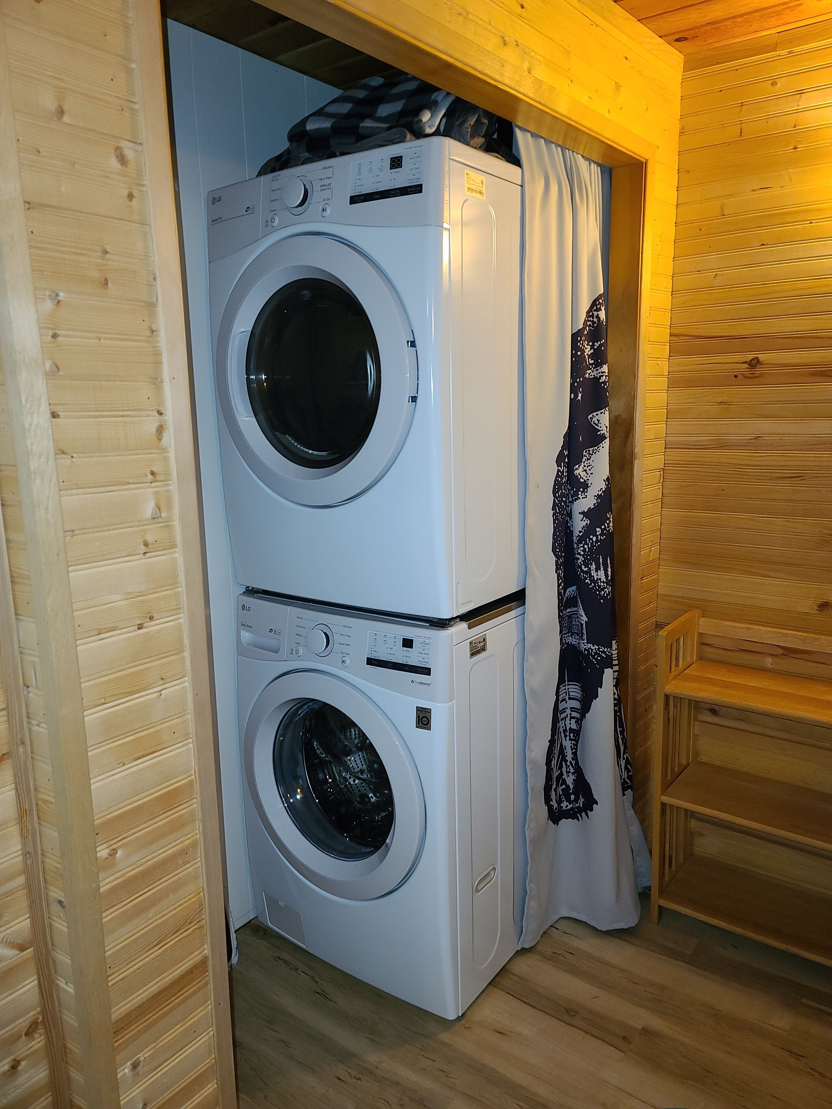 A laundry room with two stacked washing machines and a wooden bench.